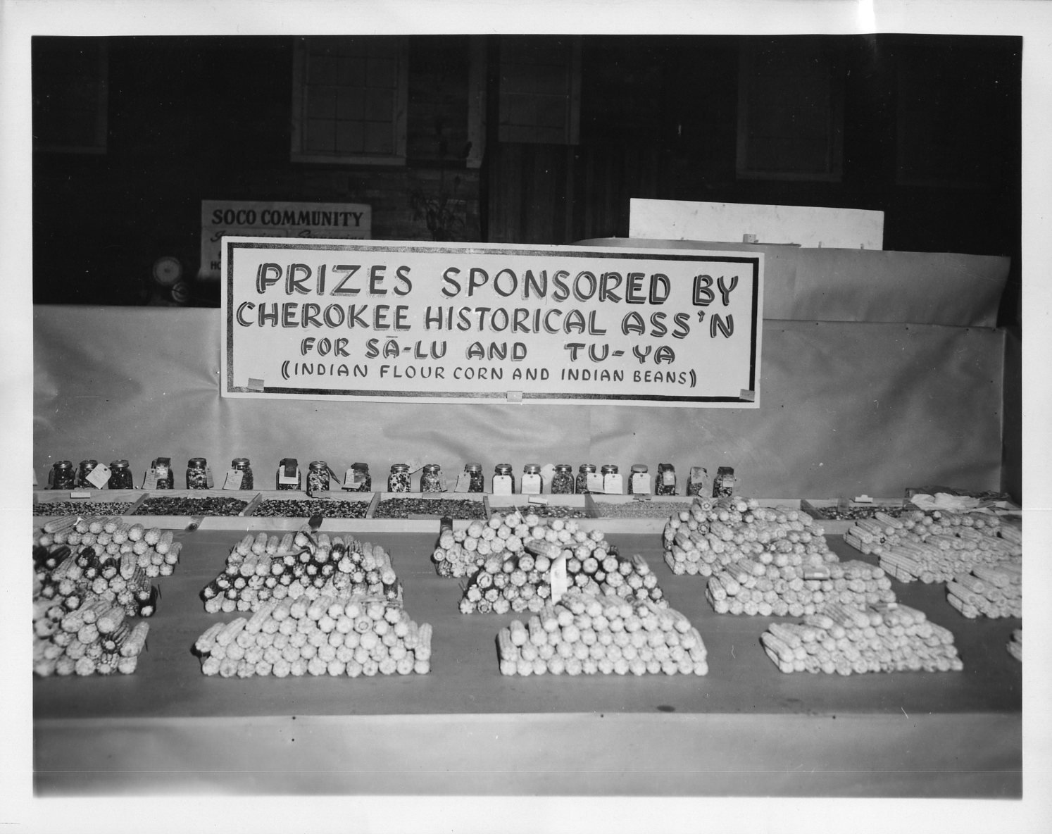 Black and white photo of corn, beans and other items on display as part of the Cherokee Historical Association sponsored contests at the 1951 Cherokee Indian Fair in Cherokee, North Carolina.