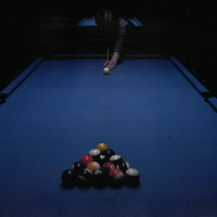 Photograph of a figure in front of a pool table, preparing to play, with pool balls in foreground